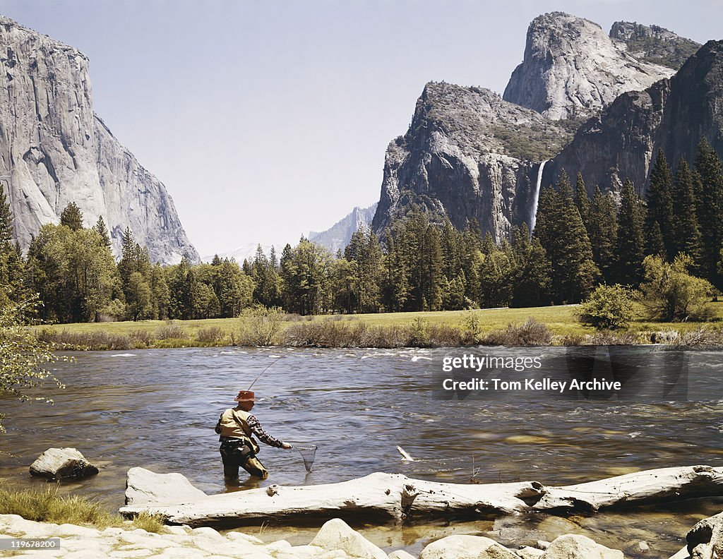 Man catching fish at riverside with mountains in background