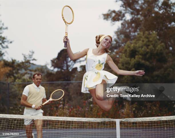 couple on tennis court, woman jumping in foreground - tennis outfit stock pictures, royalty-free photos & images