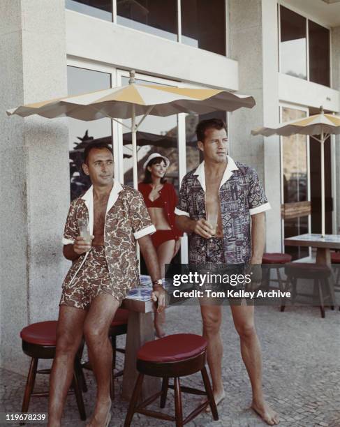 two men standing under sunshade, holding glass of drink - 1966 bildbanksfoton och bilder