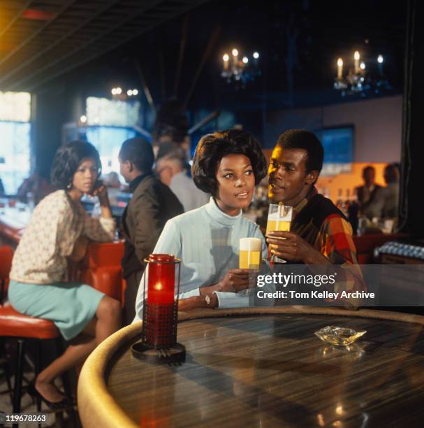 young couple sitting at table holding glass of beer - happy hour vintage stockfoto's en -beelden