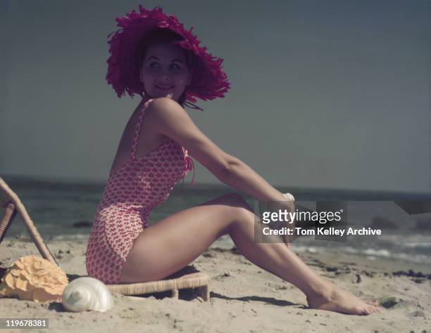 young woman sitting on lounge chair on beach, smiling - 1960 stockfoto's en -beelden