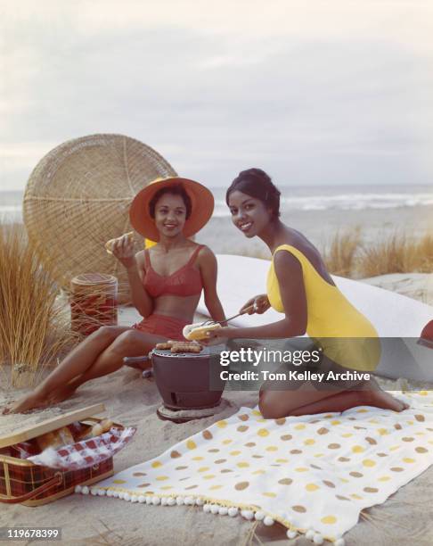 young women holding hot dog on beach, smiling - historisch stockfoto's en -beelden