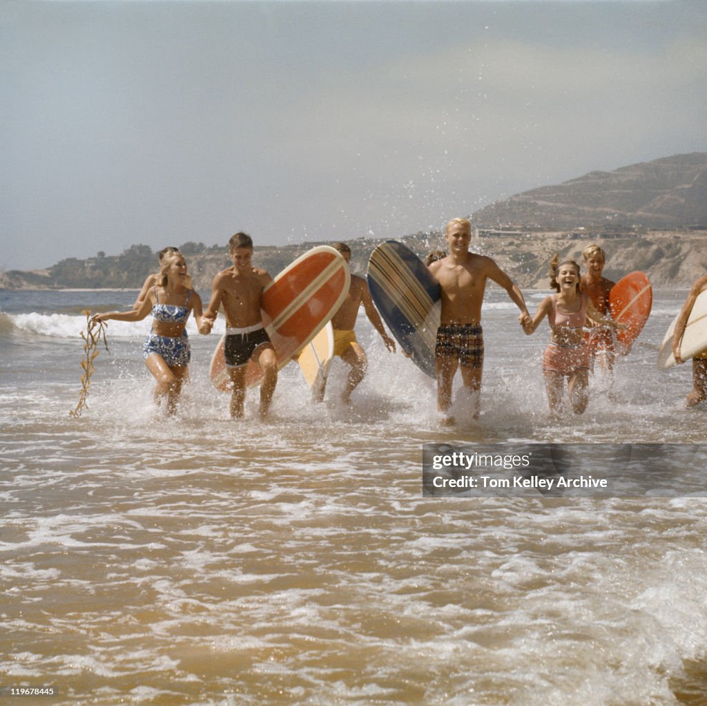 Group of surfers running in water with surfboards, smiling