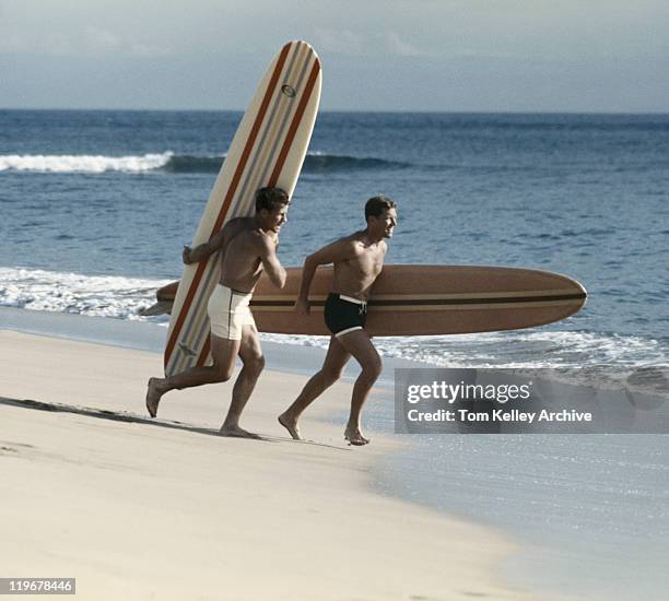 hombres jóvenes corriendo en la playa con tabla de surf - 1960 fotografías e imágenes de stock