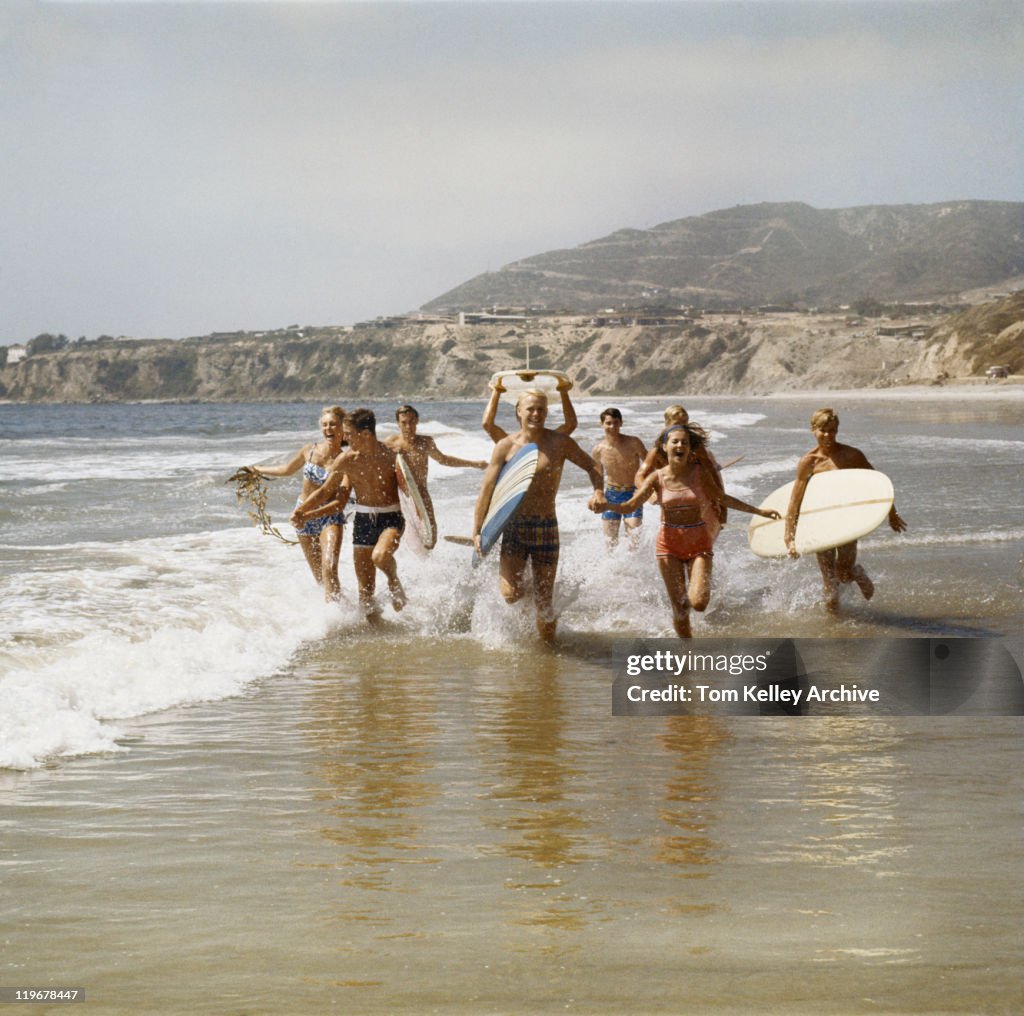 Gruppe von Surferinnen Laufen im Wasser mit Surfbrettern, Lächeln