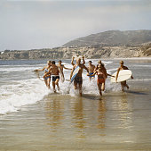 Group of surfers running in water with surfboards, smiling