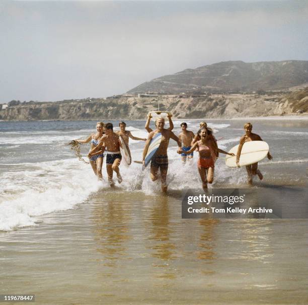 group of surfers running in water with surfboards, smiling - 60's stock pictures, royalty-free photos & images