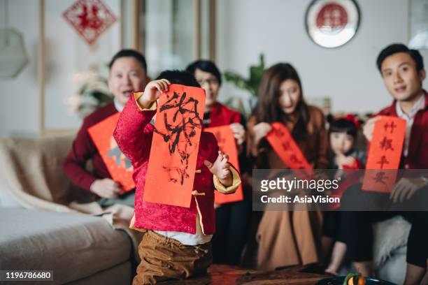 手書きの中国のファイチュン(縁起のメッセージ)を前面に持つかわいい男の子と一緒に中国の旧正月を祝うアジアの家族の3世代 - couplets ��ストックフォトと画像
