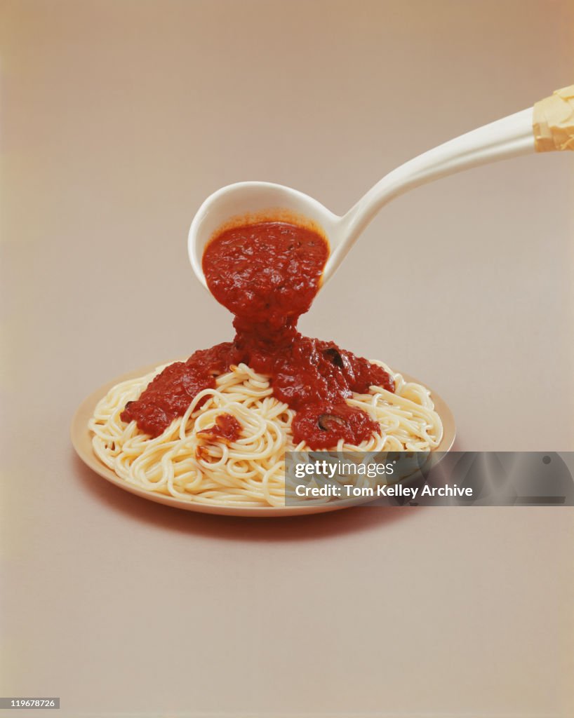 Pouring tomato sauce on noodles, close-up