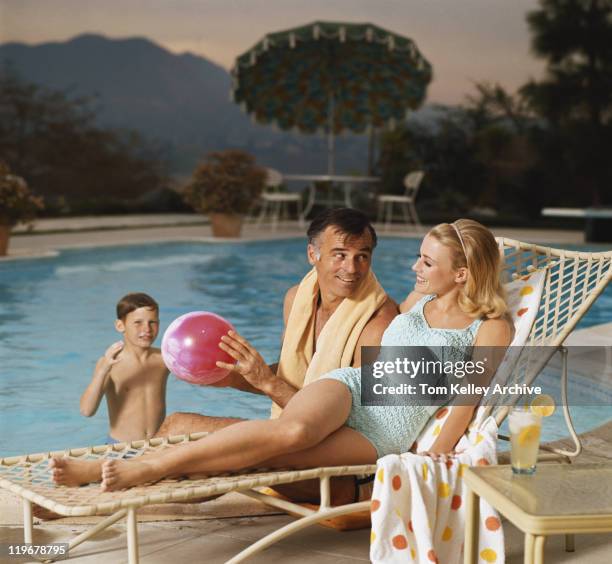 father and son playing with beach ball while mother relaxing on lounge chair, smiling - 1968 stock pictures, royalty-free photos & images