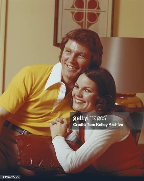 couple sitting with cushion, smiling - 1973 stockfoto's en -beelden