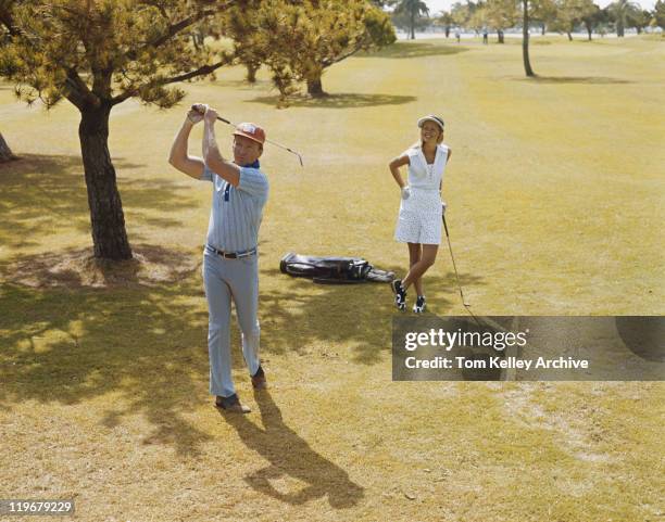 mature couple playing golf, man swinging golf club - 1973 stockfoto's en -beelden