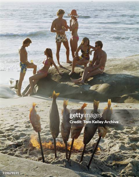 casais na praia com peixes em primeiro plano no fogo - 1973 - fotografias e filmes do acervo