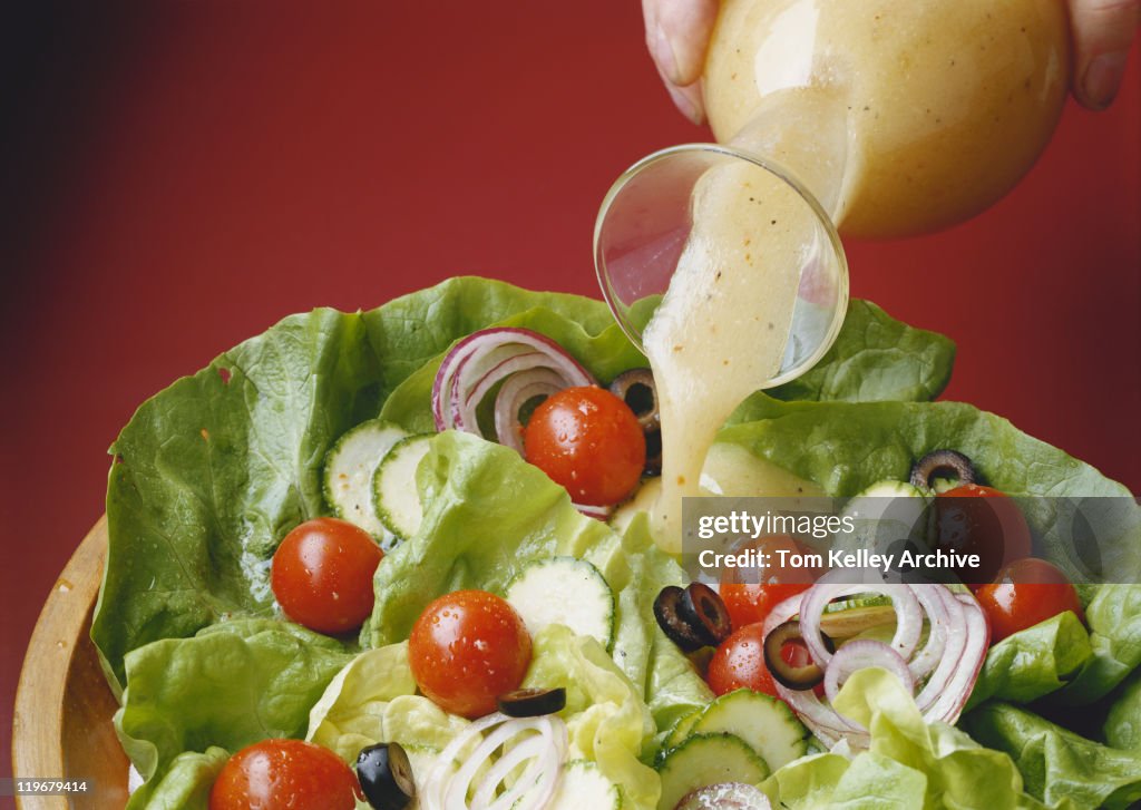 Pouring salad dressing on salad, close-up