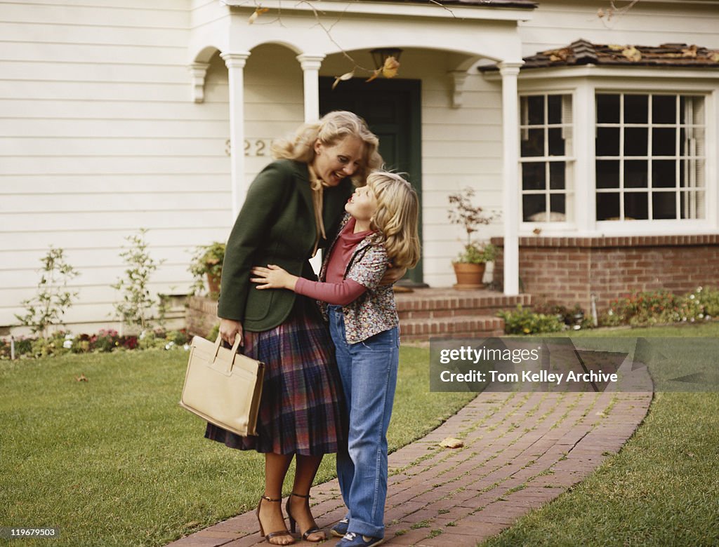 Mother embracing her daughter outside house on garden path