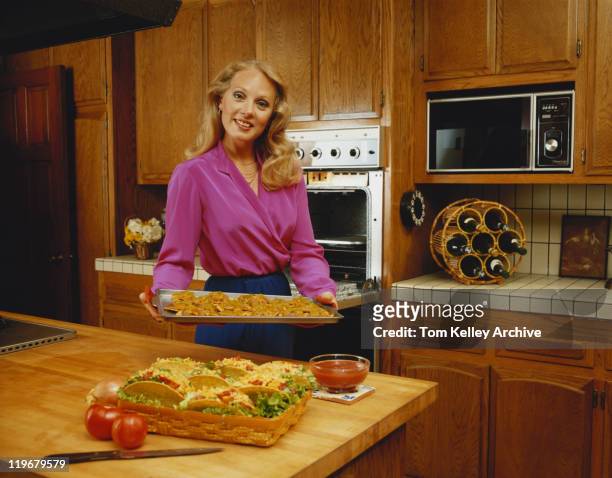 young woman holding baking tray, smiling, portrait - anno 1980 foto e immagini stock