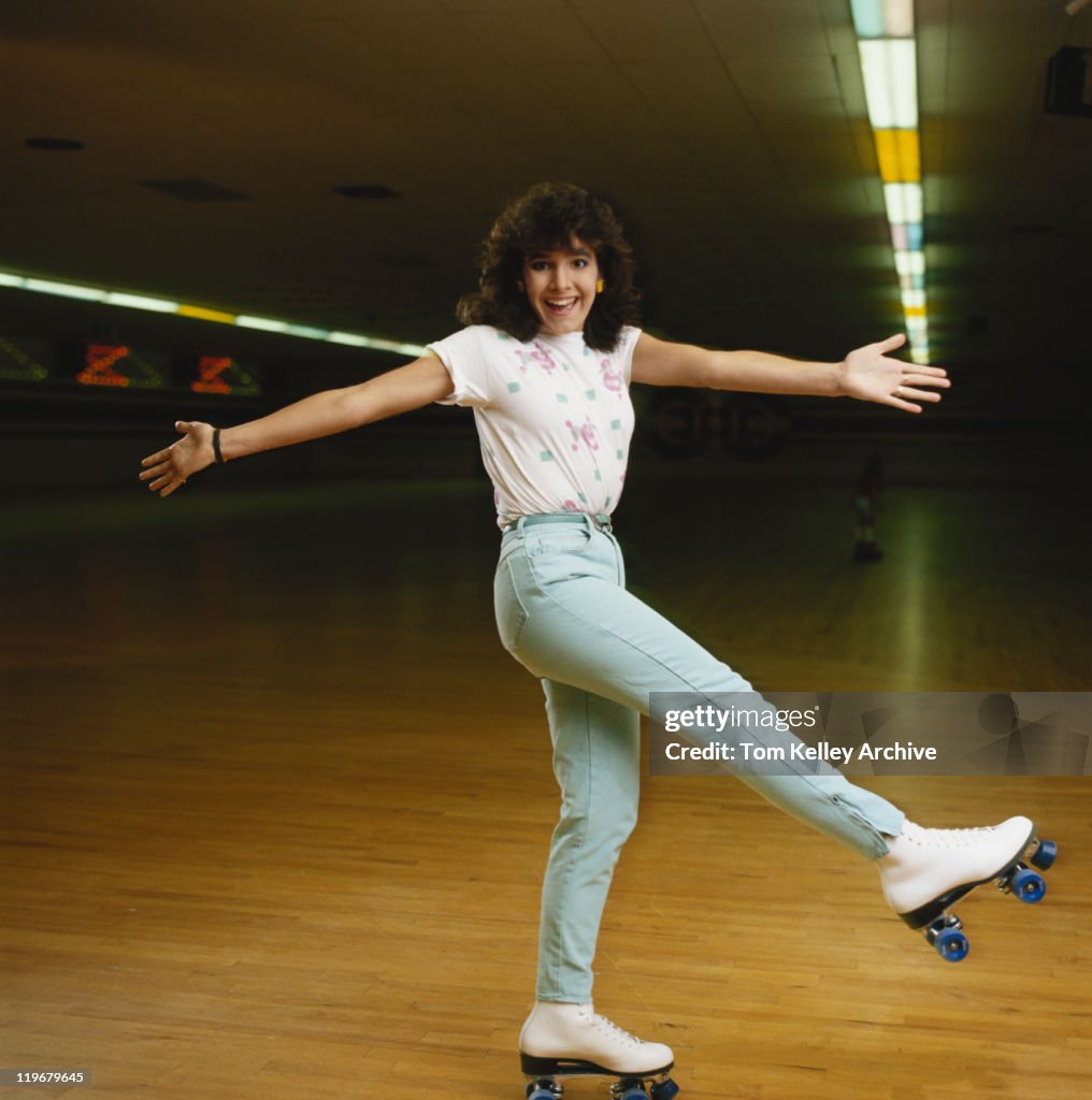 Young woman roller skating on wooden floor, smiling, portrait