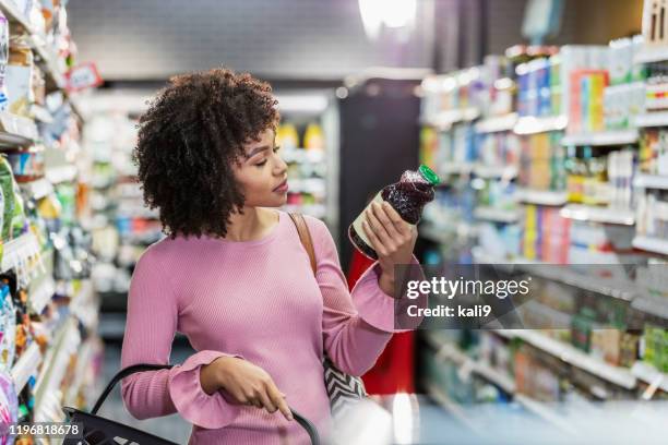 jeune femme afro-américaine faisant des emplettes dans le supermarché - information nutritionnelle photos et images de collection