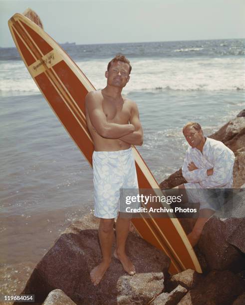 Young men with surfboard on rocks at beach, smiling