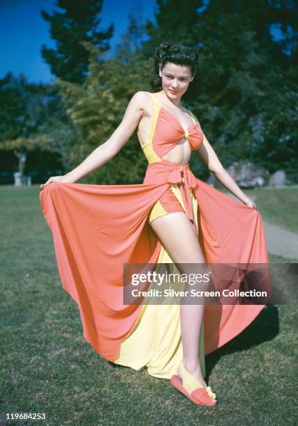 Gene Tierney , US actress, wearing a pink-and-yellow bathing costume, with a pink-and-yellow sarong and matching slippers, circa 1940.