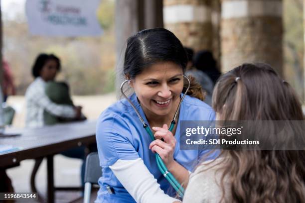 enfermera voluntaria sonríe mientras revisa a una niña en la clínica del parque - children charity fotografías e imágenes de stock