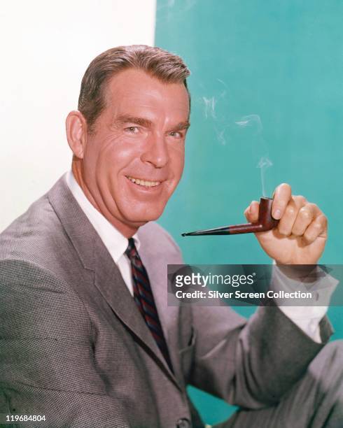 Fred MacMurray , US actor, smoking a pipe and wearing a grey suit, white shirt and a red-blue-and-black striped tie, in a studio portrait, against a...