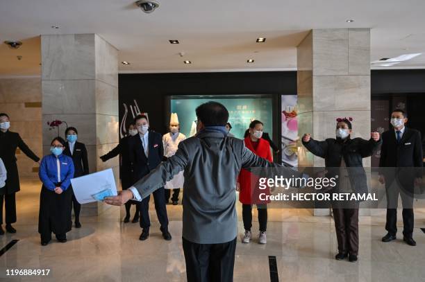 Hotel workers wearing protective masks exercise in the lobby during a staff briefing about how to implement new regulations concerning the current...