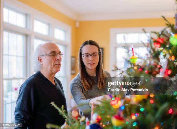 un anciano de 73 años, un padre, decorando un árbol de navidad junto con su hija adulta, una joven de 27 años. - 26 years old fotografías e imágenes de stock