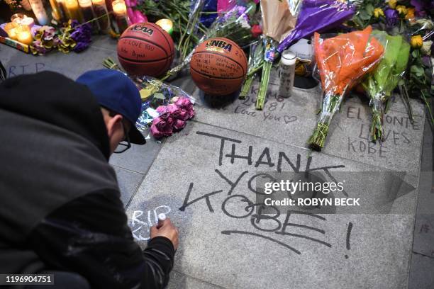 Man writes a message on the pavement near a makeshift memorial as fans gather to mourn the death of NBA legend Kobe Bryant, who was killed along with...