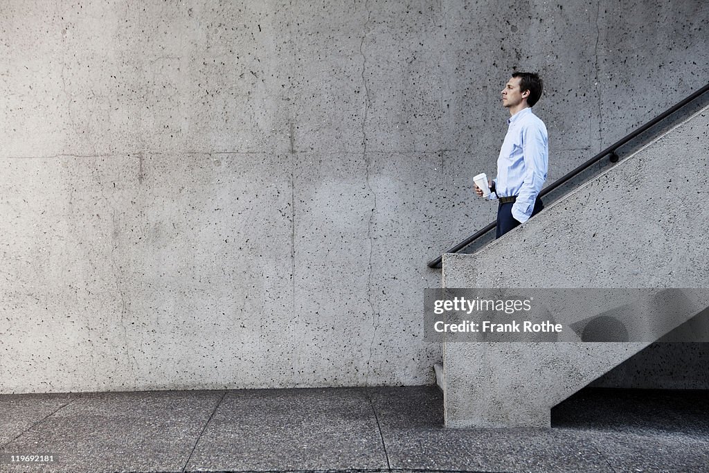 Man with cup of coffee walking down concrete stair