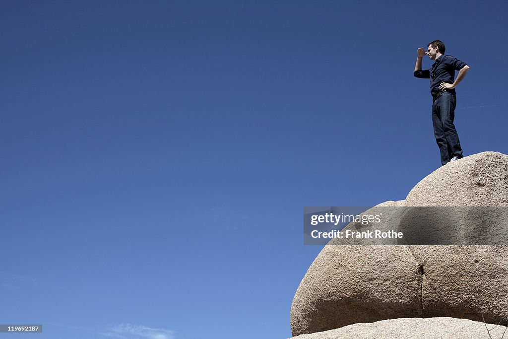 A man outdoor on a big stone overlooking the scene