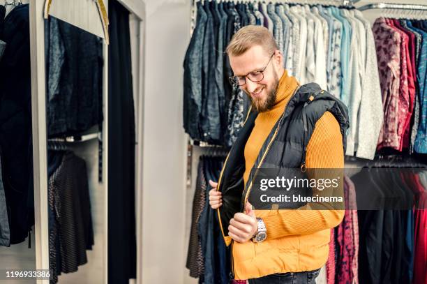 un hombre sonriente comprando ropa en los grandes almacenes. - chaleco fotografías e imágenes de stock