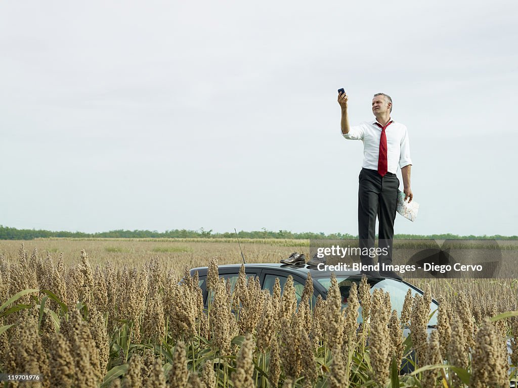 Caucasian businessman on top of car in field looking at gps device