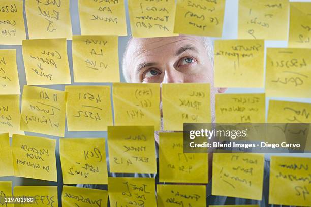 caucasian businessman looking at adhesive notes on wall - mann liste stock-fotos und bilder