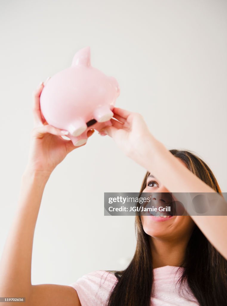 Hispanic teenage girl lifting piggy bank