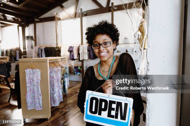 mixed race woman putting open sign on door - small business saturday stock pictures, royalty-free photos & images
