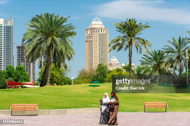 kvinna som går i parken. i bakgrunden den moderna skyline i doha-huvudstaden i qatar - persian gulf bildbanksfoton och bilder