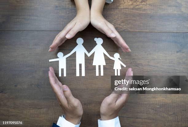 close up of female and male hands protecting a paper chain family. top view - familie schutz stock-fotos und bilder