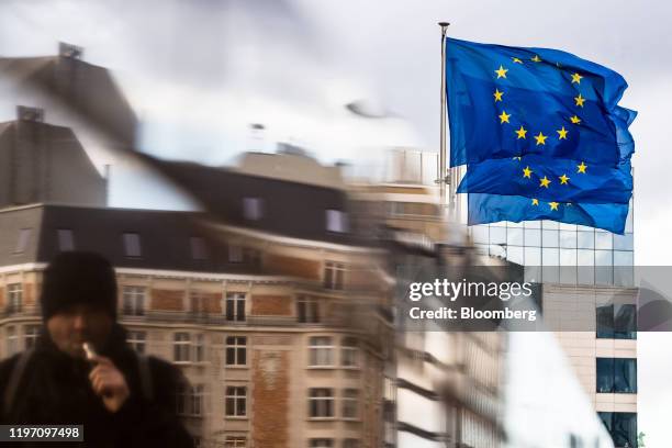 Pedestrian vapes near European Union flags flying outside the Berlaymont building, headquarters of the European Commission , in Brussels, Belgium, on...