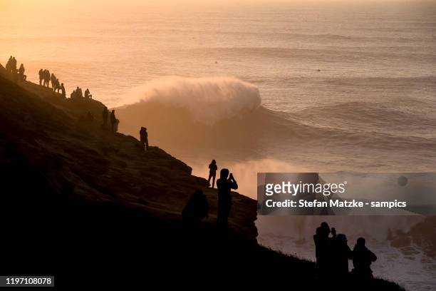 Spectators watch surfers during the sunset on December 9, 2019 in Nazare, Portugal.