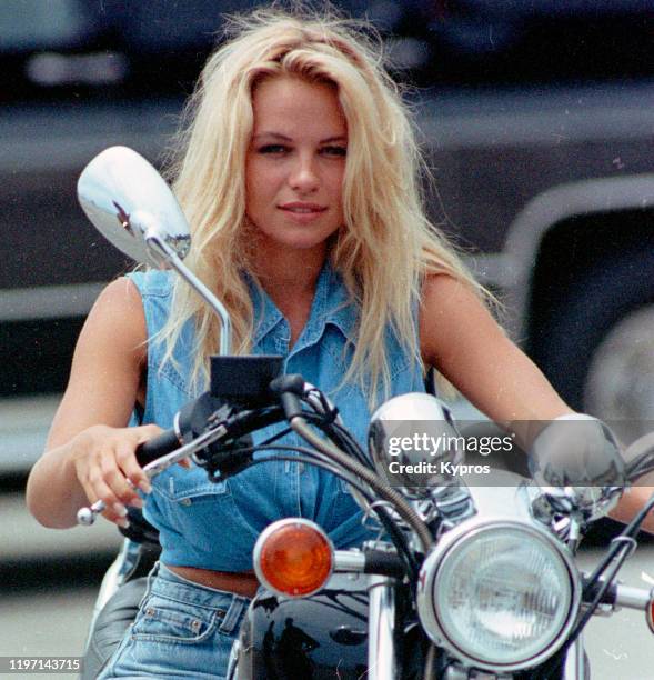 American actress Pamela Anderson on a motorcycle in denim, circa 1990.