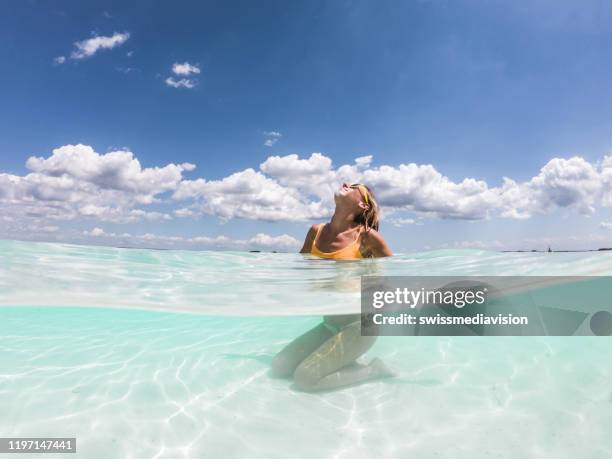scatto subacqueo di donna che si rilassa sulla spiaggia idilliaca - half underwater foto e immagini stock