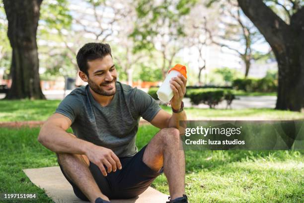 joven haciendo un batido de proteínas en el parque - shaking fotografías e imágenes de stock