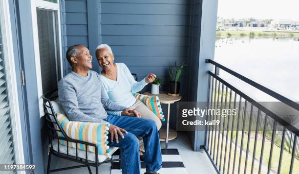 senior couple relaxing on porch, holding hand, laughing - senior couple stock pictures, royalty-free photos & images