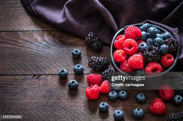 gemengde biologische bessen op een rustieke houten tafel - bowl of blueberries stockfoto's en -beelden