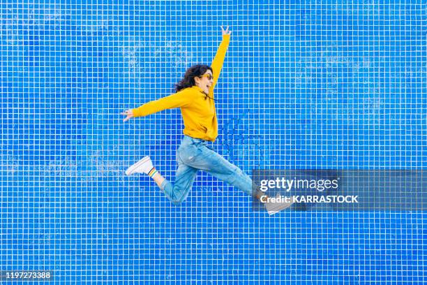 woman jumping in front of a blue background - happy jumping photos et images de collection