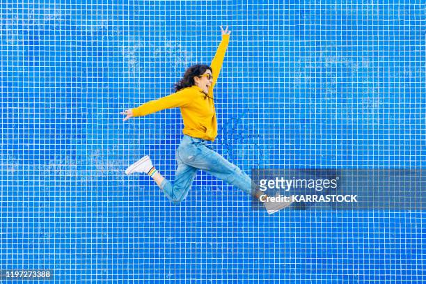 woman jumping in front of a blue background - saltare foto e immagini stock