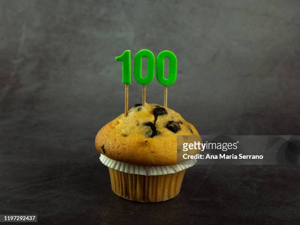 100th birthday candles in a cupcake with chocolate pieces on a dark background - 100th anniversary fotografías e imágenes de stock