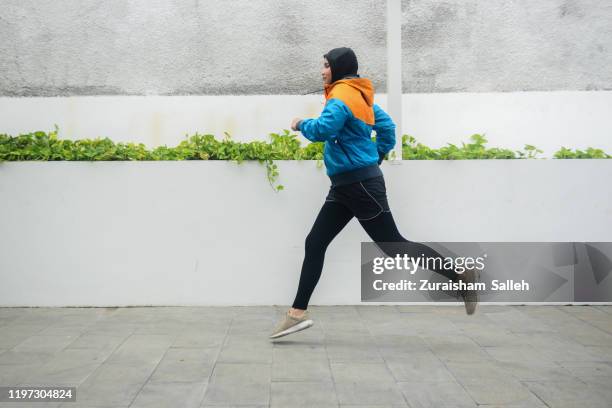 junge asiatische muslimische sportlerin in hijab läuft auf joggingstrecke - malay hijab stock-fotos und bilder