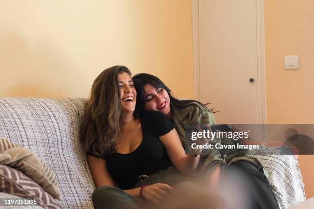 two young women are looking the tv on the couch of her house - command sisters photos et images de collection